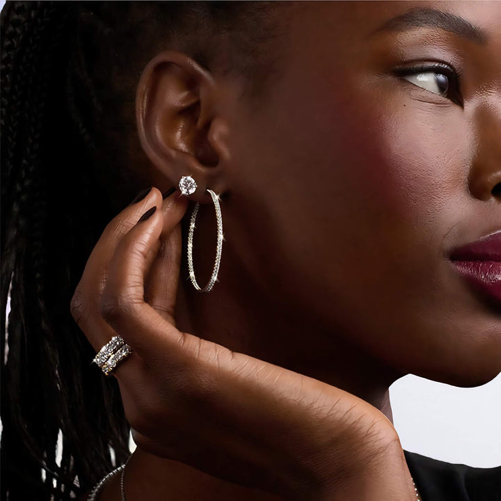 Close-up of a woman wearing diamond earrings and a ring. Lab-grown diamond martini (3-prong) stud earrings, 1.50 ctw, 14K yellow gold, on model.